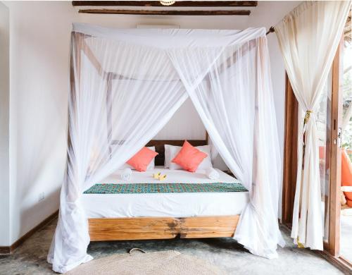 a bedroom with a canopy bed with red pillows at Bahati Sunset Bungalows Michamvi in Michamvi