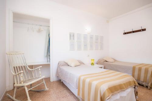 a white bedroom with two beds and a chair at Can Manuel in Felanitx