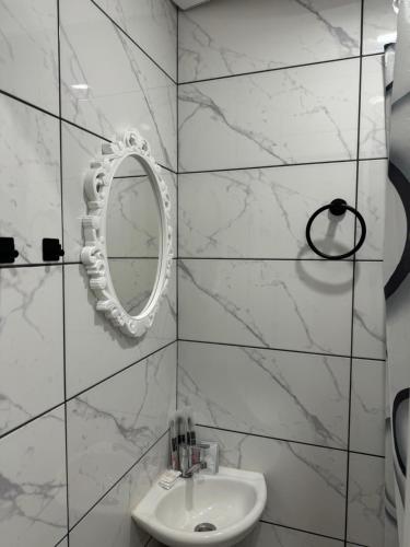 a white tiled bathroom with a sink and a mirror at Уютные 2х комнатные апартаменты на юбилейной in Uralsk