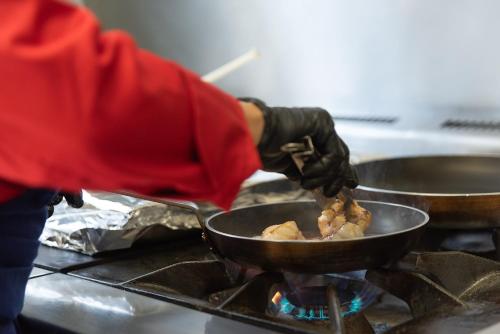 a person cooking food in a pan on a stove at hôtel TY RU in Riec-sur-Bélon
