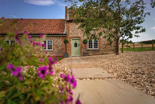 a brick house with a green door and some flowers at Brook Cottage in Kelling