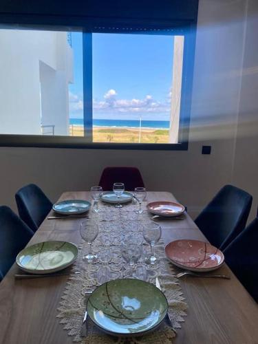 a wooden table with plates and wine glasses on it at Magnifique Appart Tanger Vue Mer Plage à 100m Calme et Nature in Tangier