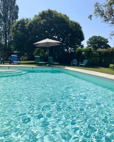 a swimming pool with an umbrella and chairs at Wisteria Gites in Saint-Denis-de-Gastines