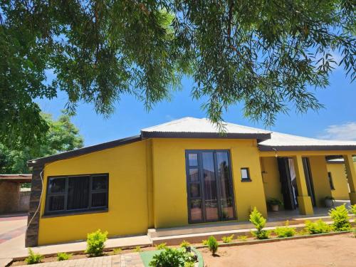 a yellow house with a tree at Thee Agolo Guesthouse in Vryburg