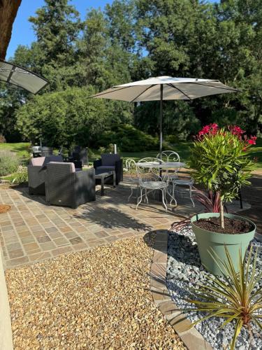un patio avec une table, des chaises et un parasol dans l'établissement Gîte du Moulin au bord de l eau, à Vernouillet