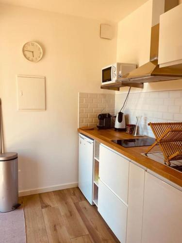 une cuisine avec des placards blancs et une horloge murale dans l'établissement L'annxe de Pibrac, à Brax