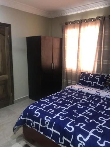a bedroom with a bed with a blue comforter and a window at Serene 2 bed with Wi-Fi and AC in Madina