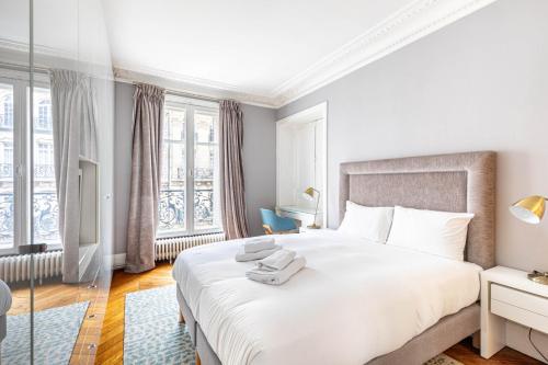 - une chambre blanche avec un grand lit blanc et des fenêtres dans l'établissement GuestReady - Appartement Spacieux et Élégant, à Paris