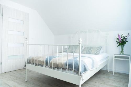 a white bedroom with a white bed and a vase of flowers at Domki Wierzbówka in Mielno