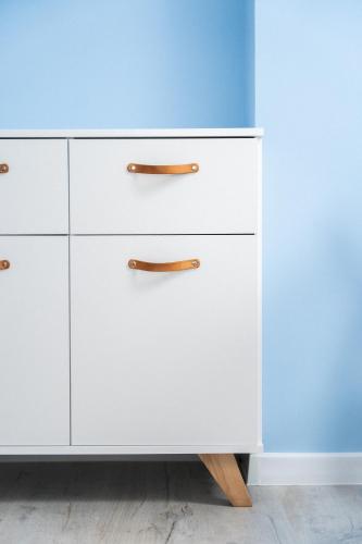 a white dresser with wooden handles next to a blue wall at Domki Wierzbówka in Mielno