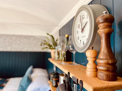 a clock sitting on top of a shelf with glasses at The Field Room - Hut on The Lizard in Helston