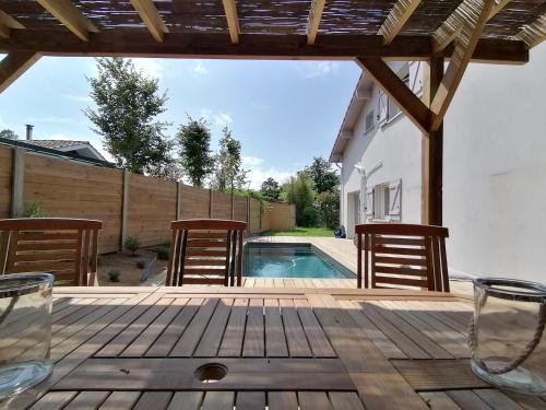 eine Holzterrasse mit Stühlen und einem Pool in der Unterkunft Oïhana Villa & Suites - Piscine chauffée - 4km de la plage in Labenne