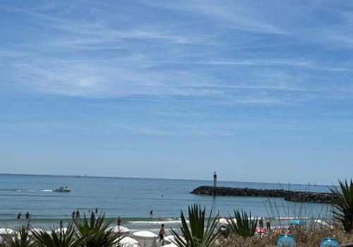 une plage avec des gens dans l'eau et une jetée dans l'établissement Studio Miroir - Héliopolis D 72 - Luxe - 4 personnes, au Cap d'Agde