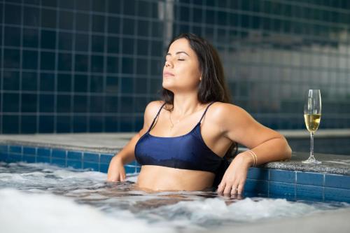 a woman in a bathing suit in a swimming pool with a glass of wine at H2 Platinum Lourdes in Belo Horizonte