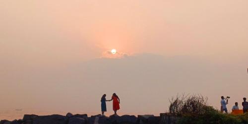 two people standing on rocks with the sunset in the background at DIVINE BEACH INN - The sea shore hotel in Puducherry