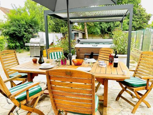 a wooden table with chairs and a grill under an umbrella at Appart Lumineux avec Jardin et Jacuzzi - Chambre Parentale - Full AC - Proche - CDG - Stade de France - Parc des Expositions in Le Blanc-Mesnil