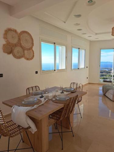 a wooden table in a room with chairs and windows at Tanger, Vue Mer Panoramique in Noûnouech