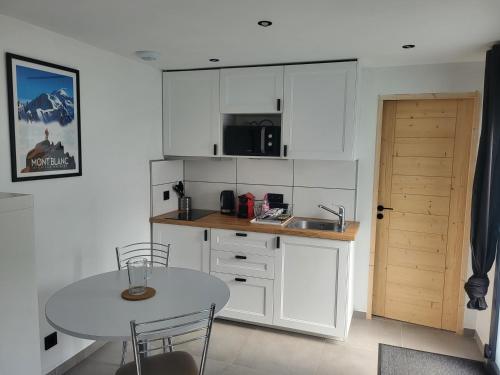 une cuisine avec des armoires blanches, une table et un évier dans l'établissement Studio Saint Antoine Les Houches, aux Houches
