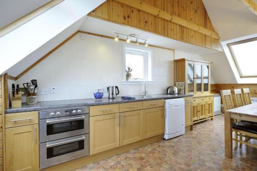 cocina grande con armarios de madera y electrodomésticos de acero inoxidable en Windyhill Cottage en Achiltibuie
