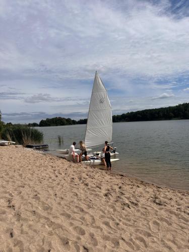 a group of people sitting on a beach with a sail boat at Nad Sunowem Lake House in Chrzanowo