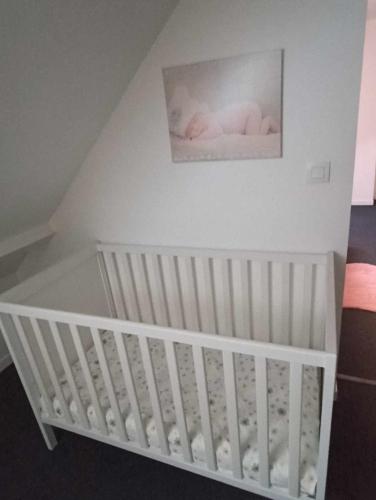 a white baby crib with a picture on the wall at maison 2 chambres 4 lits 15mn Aéroport de Beauvais 5mn du château de la trye in Hermes