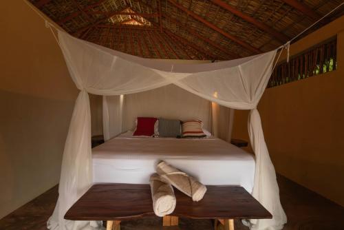 a bed with a canopy with two benches in a room at Cabanas Adobe Frente Al Mar in Puerto Escondido