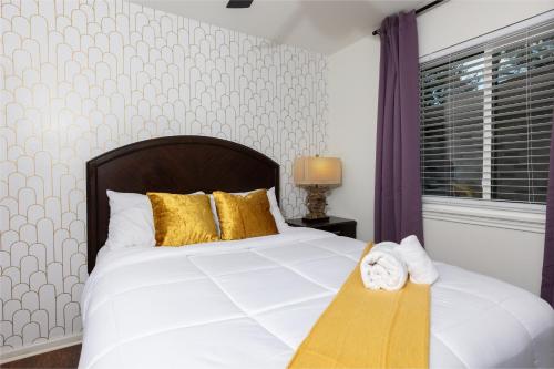 a bedroom with a white bed with gold pillows and a window at Cozy, Round Rock Retreat, Modern, Sleeps 10 in Round Rock