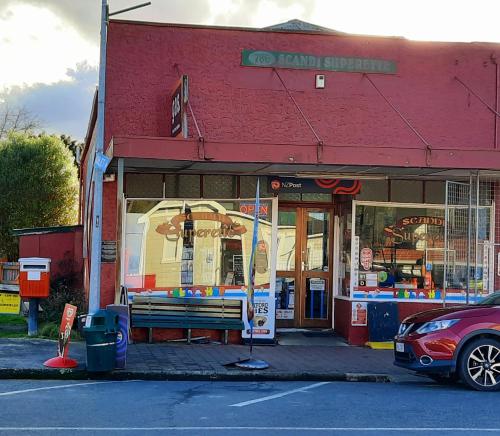 a red building with a bench in front of a store at The Old Dairy Factory in Norsewood