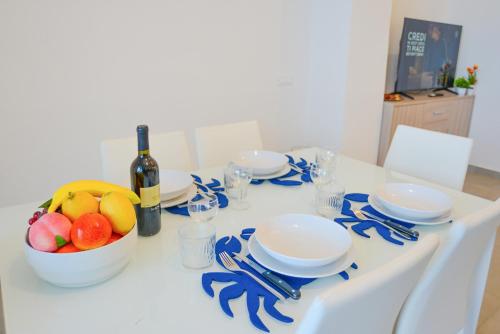 a white table with a bowl of fruit and a bottle of wine at Sopra le Onde VADOALMARE Immobiliare in Vado Ligure