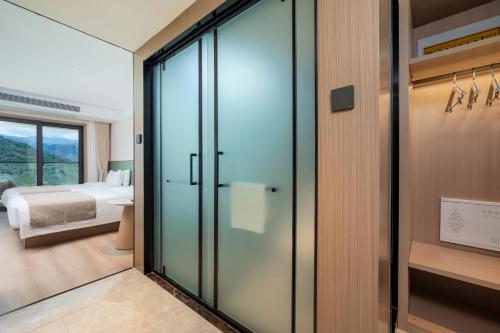 a bedroom with a bed and a glass door leading to a bathroom at Huangshan Muxin Hotel in Tanjiaqiao