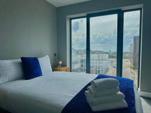 a bedroom with a bed with blue pillows and a large window at Monarchs Quay Arena Apartments by Happy Days in Liverpool