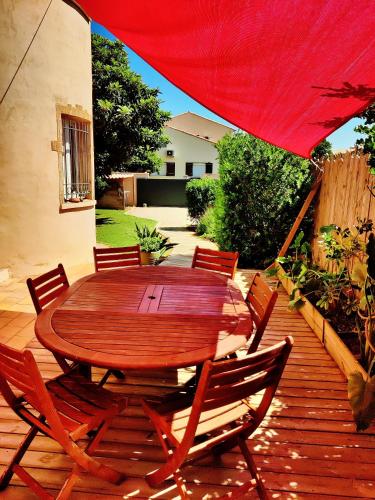 une table et des chaises en bois sur une terrasse avec un parasol rouge dans l'établissement Villa Douceur de Vivre à 15 min de la plage, à Villeneuve-lès-Maguelone