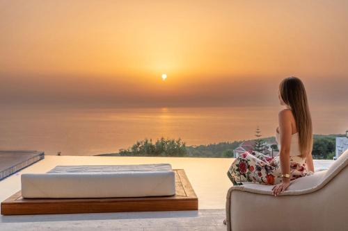 a woman sitting on a bed looking at the sunset at CASTA DIVA Luxury Accommodation in Fiskardho