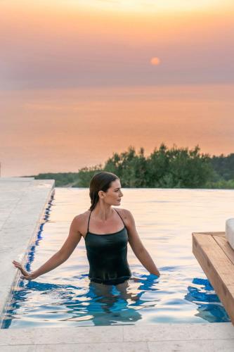 a woman in a swimming pool with the sunset in the background at CASTA DIVA Luxury Accommodation in Fiskardho