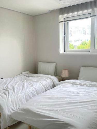 two beds in a white room with a window at Asla stay in Incheon