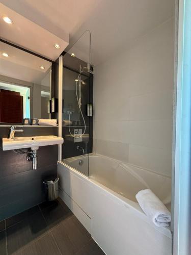 une salle de bain avec une baignoire, un lavabo et un miroir dans l'établissement Kyriad Bordeaux Lormont, à Lormont