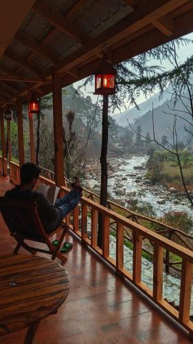 a man sitting in a chair on a porch overlooking a river at The Riverwalk in Gushaini