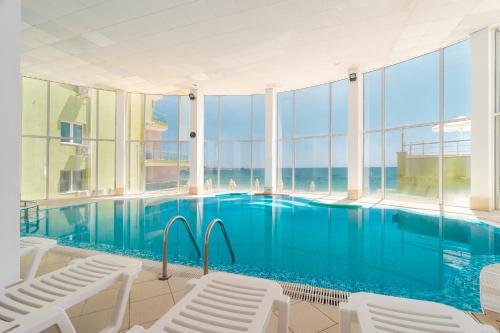 a large swimming pool with white chairs and windows at MPM Hotel Arsena - Ultra All Inclusive in Nesebar