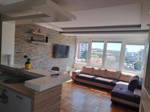 a living room with a couch and a kitchen with windows at Apartman Centar V in Smederevska Palanka