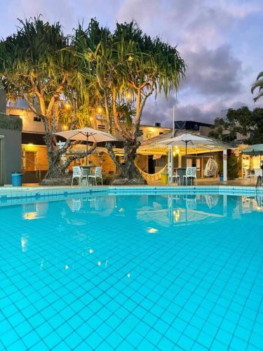 a large blue swimming pool with umbrellas and trees at Pousada Corais Barra in Barra de São Miguel