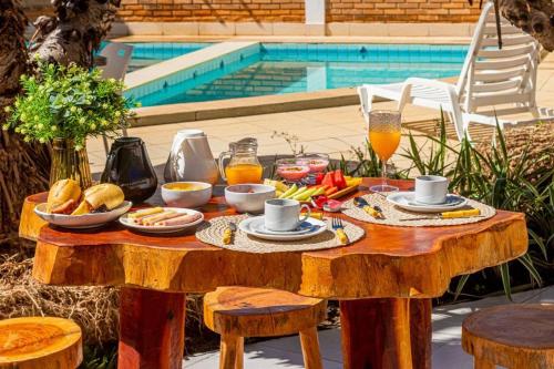 a wooden table with breakfast foods on it next to a pool at Pousada Corais Barra in Barra de São Miguel