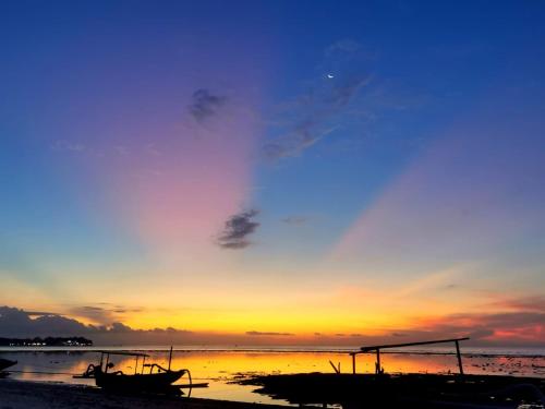 a sunset on the beach with two boats on the shore at Exotic house in Gili Meno