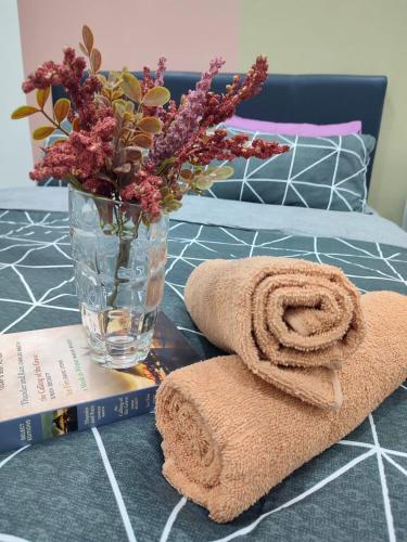 ein Handtuch und eine Vase mit Blumen und einem Buch in der Unterkunft Rara Homestay Kuala Kangsar in Kuala Kangsar