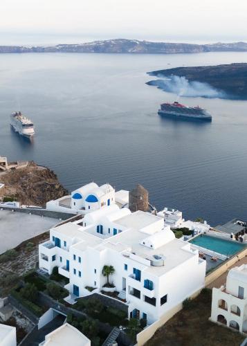 a large white building next to the water with a cruise ship at Aeifos Boutique Hotel in Imerovigli