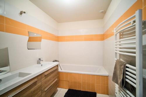 La salle de bains orange et blanche est pourvue d'un lavabo et d'une baignoire. dans l'établissement Corps de Ferme Idyllique en Bord de Rance, à Pleudihen-sur-Rance