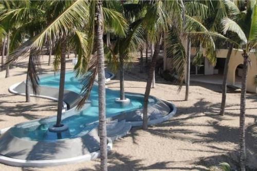 a swimming pool with palm trees in the sand at Hermosa villa a pie de playa in Barra de Potosi
