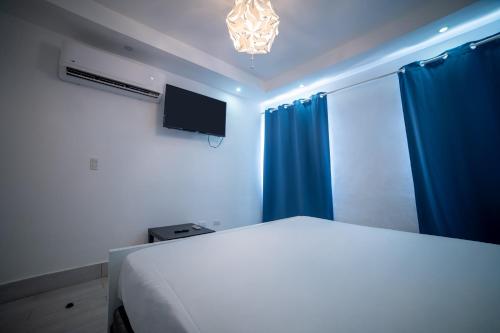 a bedroom with a bed and a tv and blue curtains at La Yarolina in Punta Cana