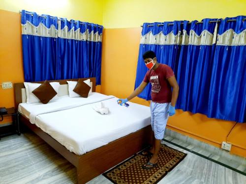 a man standing next to a bed in a room at Couple Friendly Rooms in kolkata