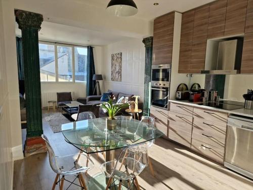 une cuisine avec une table en verre et un salon dans l'établissement Appartement atypique clair et spacieux avec jardin, à Trouville-sur-Mer