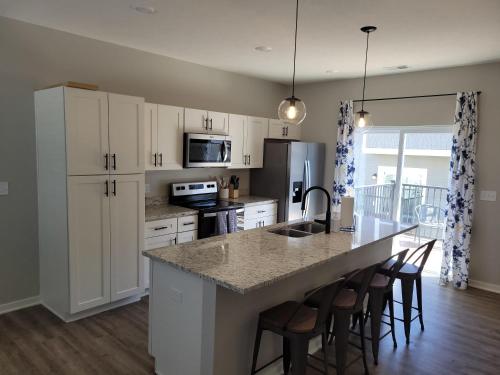 a kitchen with white cabinets and a island with bar stools at The Cottonwood at Coventry Rows in Omaha